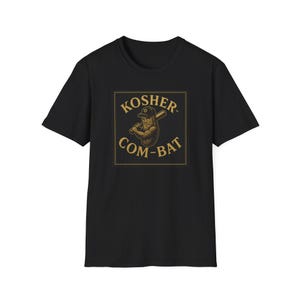 May include: Black t-shirt with a graphic featuring a cartoon pickle holding a baseball bat. The text "KOSHER COM-BAT" is displayed in a square frame with gold lettering. The pickle is wearing a baseball cap.