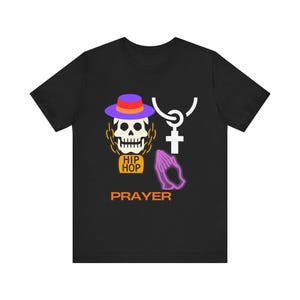 May include: Black t-shirt with a purple and orange skull wearing a purple hat, a white cross, a purple praying hand, and the words "Hip Hop" and "Prayer".