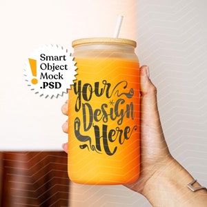 May include: A person's hand holding a clear glass jar with a bamboo lid and a straw. The jar is filled with a bright orange liquid and has the text "your design here" written on it.