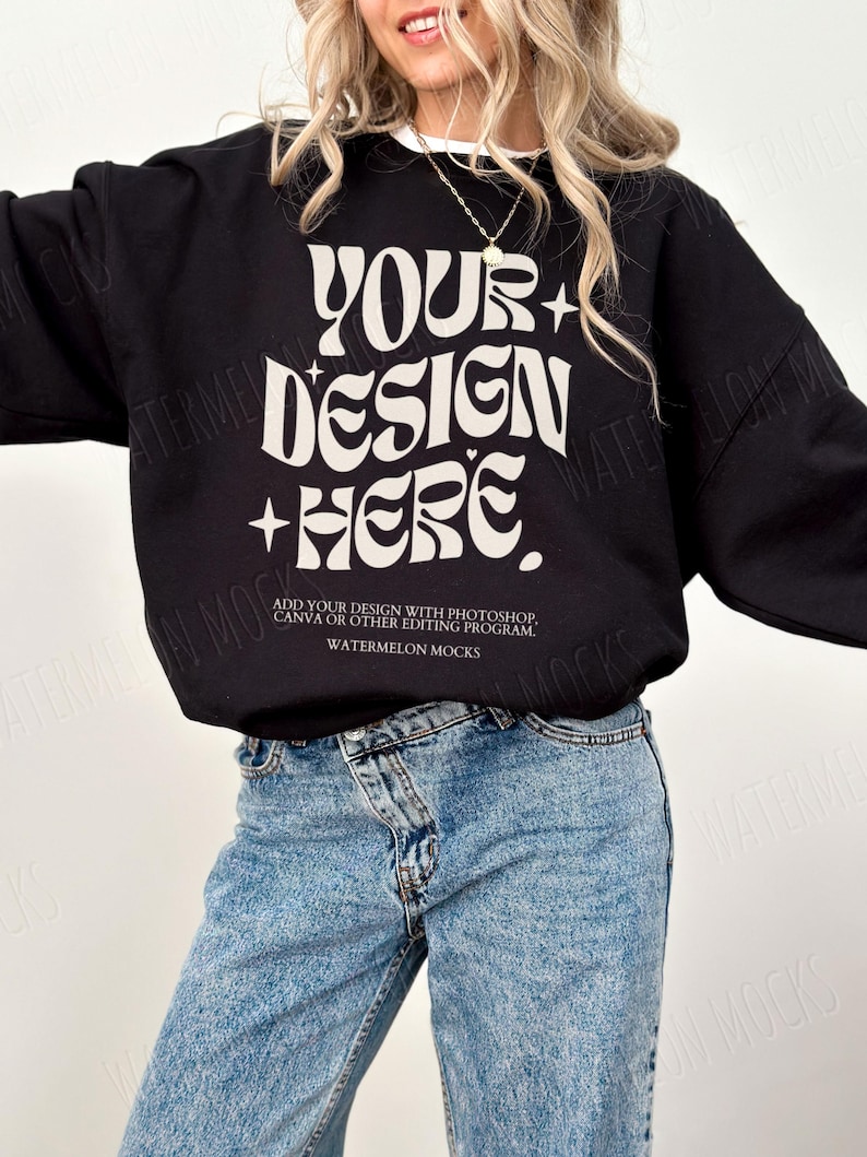 May include: A black sweatshirt with the text "YOUR+DESIGN+HERE" in white. The text is in a retro font style. The sweatshirt is being modelled by a person wearing blue jeans.