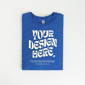 Pu&ograve; includere: Una maglietta blu piegata con il testo "YOUR DESIGN HERE" in bianco. Il testo &egrave; in uno stile di font retr&ograve;. Il testo sotto il design dice "ADD YOUR DESIGN WITH PHOTOSHOP, CANVA OR OTHER EDITING PROGRAM WATERMELON MOCKS".