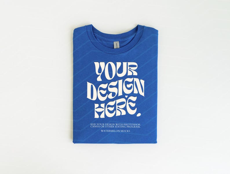 Pu&ograve; includere: Una maglietta blu piegata con il testo "YOUR DESIGN HERE" in bianco. Il testo &egrave; in uno stile di font retr&ograve;. Il testo sotto il design dice "ADD YOUR DESIGN WITH PHOTOSHOP, CANVA OR OTHER EDITING PROGRAM WATERMELON MOCKS".