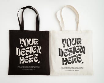 May include: Two tote bags, one black and one off-white, each featuring the text "YOUR DESIGN HERE." in a bold, wavy font. Below the main text, smaller print reads "ADD YOUR DESIGN WITH PHOTOSHOP, CANVA OR OTHER EDITING PROGRAM. WATERMELON MOCKS."