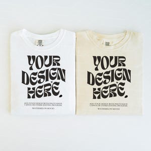 Könnte beinhalten: Zwei T-Shirts, eines in Weiß und eines in Creme, jeweils mit dem schwarzen Schriftzug "YOUR DESIGN HERE" in einer geschwungenen Schriftart. Darunter steht in kleinerer Schrift "ADD YOUR DESIGN WITH PHOTOSHOP, CANVA OR OTHER EDITING PROGRAM" und "WATERMELON MOCKS".