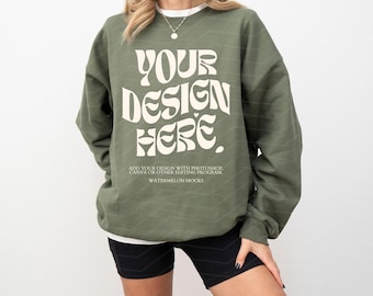 Op de afbeelding: Een olijfgroen sweatshirt met ronde hals en de crèmekleurige tekst "YOUR DESIGN HERE." en daaronder kleinere tekst: "ADD YOUR DESIGN WITH PHOTOSHOP, CANVA OR OTHER EDITING PROGRAM. WATERMELON MOCKS." Het sweatshirt heeft lange mouwen.