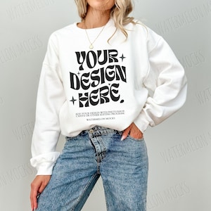 May include: White sweatshirt with a black retro font design that says "YOUR DESIGN HERE."  The text is on a white sweatshirt with long sleeves. The model is wearing blue jeans.