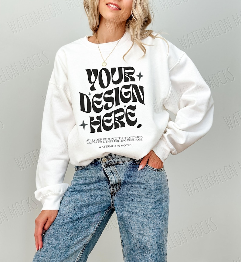 May include: White sweatshirt with a black retro font design that says "YOUR DESIGN HERE."  The text is on a white sweatshirt with long sleeves. The model is wearing blue jeans.