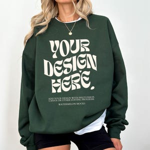 May include: A dark green sweatshirt with the text "YOUR DESIGN HERE" in a retro font. The text is in a cream colour. The sweatshirt has a crew neck and long sleeves. The text below the design reads "ADD YOUR DESIGN WITH PHOTOSHOP, CANVA OR OTHER EDITING PROGRAM. WATERMELON MOCKS."