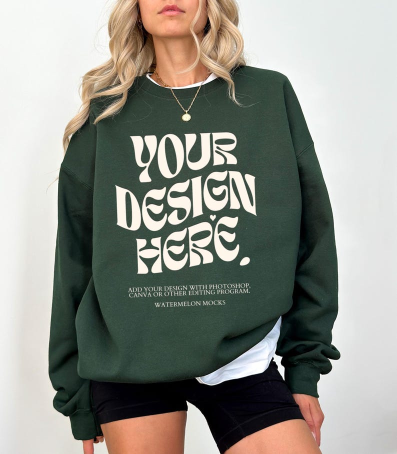 May include: A dark green sweatshirt with the text "YOUR DESIGN HERE" in a retro font. The text is in a cream colour. The sweatshirt has a crew neck and long sleeves. The text below the design reads "ADD YOUR DESIGN WITH PHOTOSHOP, CANVA OR OTHER EDITING PROGRAM. WATERMELON MOCKS."