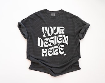 May include: A charcoal gray short-sleeve t-shirt with a crew neckline and rolled sleeves. The center of the shirt features the white text "YOUR DESIGN HERE" in a bold, wavy, retro-inspired font style against the dark fabric background.