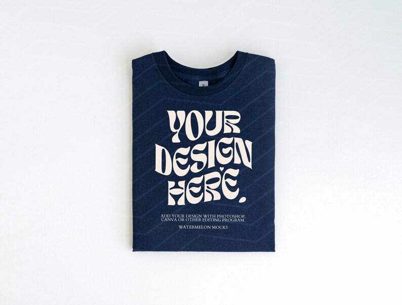 Pu&ograve; includere: Una maglietta blu navy piegata con una grafica bianca che dice "YOUR DESIGN HERE". Il testo &egrave; in uno stile di font retr&ograve;. La maglietta &egrave; su uno sfondo bianco.