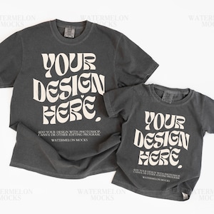 May include: Two charcoal gray t-shirts, one adult and one child size, with the text "YOUR DESIGN HERE" in a retro font. The shirts are mockups for design placement, with additional text at the bottom.