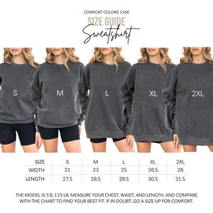 May include: A size guide for a Comfort Colors 1566 sweatshirt featuring five charcoal gray crewneck sweatshirts in sizes S, M, L, XL, and 2XL. A table displays width and length measurements in inches, ranging from 21 to 28 inches wide and 27.5 to 31.5 inches long.