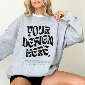 May include: A grey sweatshirt with the text "YOUR DESIGN HERE" in black. The text is in a retro font style. The text below the design reads "ADD YOUR DESIGN WITH PHOTOSHOP, CANVA OR OTHER EDITING PROGRAM. WATERMELON MOCKS."