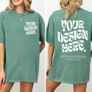 May include: A sage green short-sleeve t-shirt featuring white text on the front left chest and a larger version on the back. The text reads "YOUR DESIGN HERE" in a wavy font, with additional instructions below the back graphic.