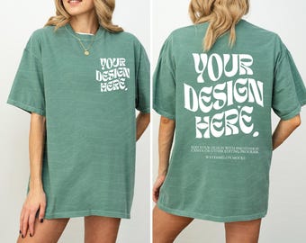May include: A sage green short-sleeve t-shirt featuring white text on the front left chest and a larger version on the back. The text reads "YOUR DESIGN HERE" in a wavy font, with additional instructions below the back graphic.