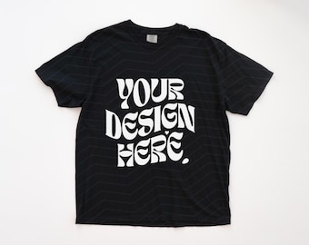 May include: A black short-sleeved t-shirt featuring the white text "YOUR DESIGN HERE" in a bold, wavy, retro-inspired font. The fabric has a subtle, repeating chevron pattern across the entire surface of the garment, including the sleeves.