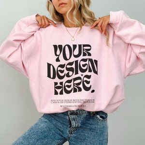 May include: A pink sweatshirt with the text "YOUR DESIGN HERE" in black retro-style lettering. The text "ADD YOUR DESIGN WITH PHOTOSHOP, CANVA OR OTHER EDITING PROGRAM. WATERMELON MOCKS" is printed below the main text.