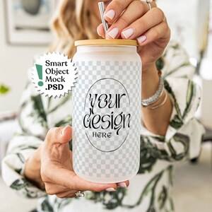 May include: A frosted glass tumbler with a bamboo lid and a metal straw. The tumbler features a light gray and white checkered pattern with a central oval frame containing the black text "YOUR DESIGN HERE". A circular badge reads "Smart Object Mock .PSD".