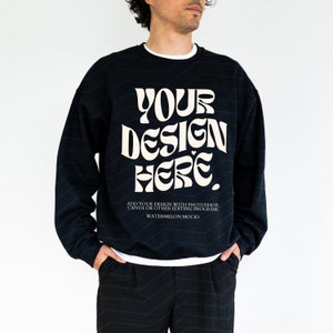 Könnte beinhalten: Ein schwarzer Pullover mit einem weißen Design, das "YOUR DESIGN HERE." lautet. Der Text ist in einer Retro-Psychedelic-Schriftart gehalten. Der Pullover hat einen Rundhalsausschnitt und lange Ärmel. Der Text unter dem Design lautet "ADD YOUR DESIGN WITH PHOTOSHOP, CANVA OR OTHER EDITING PROGRAM. WATERMELON MOCKS."