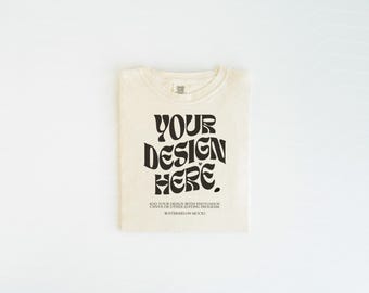 May include: A cream-colored t-shirt featuring the black text YOUR DESIGN HERE in a bold, wavy font. Below the main text, smaller black text reads ADD YOUR DESIGN WITH PHOTOSHOP, CANVA OR OTHER EDITING PROGRAM and WATERMELON MOCKS.