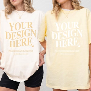 May include: Two oversized t-shirts, one ivory and one banana yellow, with the text "YOUR DESIGN HERE" printed on the front. The text is in a bold, stylized font.