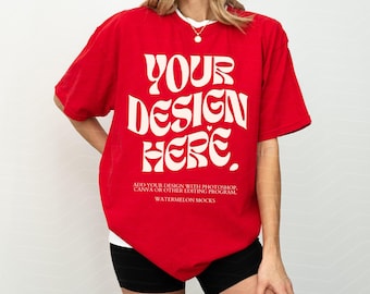 May include: A bright red short-sleeve t-shirt featuring the white text YOUR DESIGN HERE in a large, wavy font. Below this, smaller white text reads ADD YOUR DESIGN WITH PHOTOSHOP, CANVA OR OTHER EDITING PROGRAM and WATERMELON MOCKS.