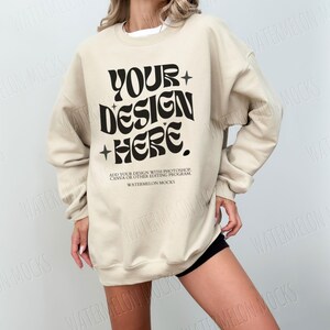 May include: A beige sweatshirt with the text "YOUR+DESIGN+HERE." in black. The text is in a retro font style. The text below the design reads "ADD YOUR DESIGN WITH PHOTOSHOP, CANVA OR OTHER EDITING PROGRAM WATERMELON MOCKS."
