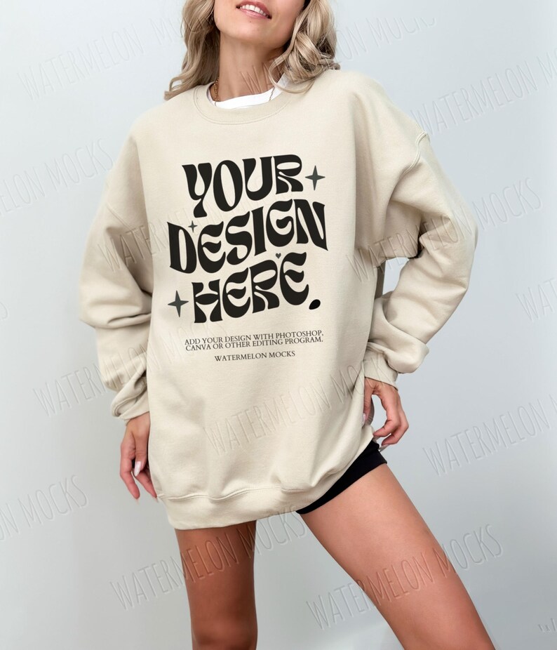 May include: A beige sweatshirt with the text "YOUR+DESIGN+HERE." in black. The text is in a retro font style. The text below the design reads "ADD YOUR DESIGN WITH PHOTOSHOP, CANVA OR OTHER EDITING PROGRAM WATERMELON MOCKS."