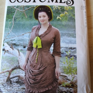 May include: A McCall's Costumes sewing pattern envelope M8189 featuring a brown dress with a small white dot pattern, a lime green bow, and lime green buttons. The dress has three-quarter sleeves, a ruffled neckline, and a ruffled hem.