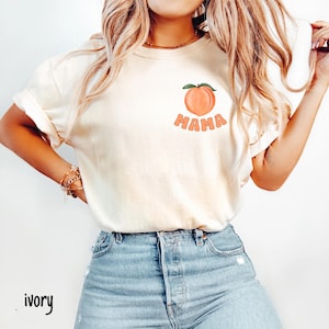 May include: A white t-shirt with a peach graphic and the word "MAMA" in peach-colored letters.