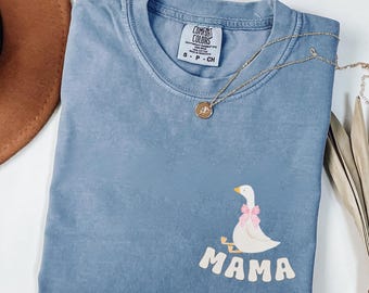 May include: A blue jean t-shirt with a white goose wearing a pink bow and the word "MAMA" printed on the front. The shirt has a distressed look and is made by Comfort Colors.