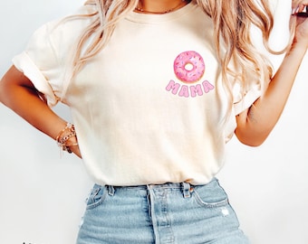 May include: Ivory-colored t-shirt featuring a pink donut graphic with the word "MAMA" below it. The shirt has rolled-up sleeves and is paired with blue jeans. The word "ivory" is printed at the bottom left.
