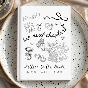 May include: A white journal with black line art illustrations and text. The cover reads "her next chapter" and "Letters to the Bride, MRS. WILLIAMS." Illustrations include hearts, flowers, rings, and a banner that says "Save the Date."
