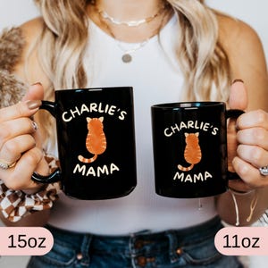 May include: Two black ceramic mugs with the text "Charlie's Mama" and a cartoon orange cat design. One mug is 15oz, the other is 11oz. Both mugs have a black handle.