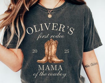 May include: Dark gray t-shirt with the text "OLIVER'S first rodeo" above a graphic of cowboy boots. Below the boots are the numbers "20" and "25" and the phrase "MAMA of the cowboy". The word "pepper" is printed in the bottom left corner.