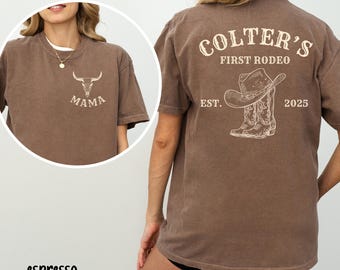 May include: Espresso-colored t-shirt with a graphic of a bull skull and the word "MAMA" on the front. The back features the text "COLTER'S FIRST RODEO" above a cowboy hat and boots design, with "EST. 2025" below.