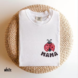 May include: White t-shirt with a red and black ladybug graphic and the word "MAMA" printed below it.