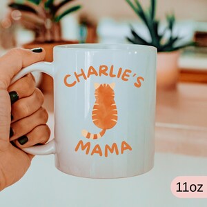 May include: White ceramic mug with the text "Charlie's Mama" in orange. The mug features an orange cat illustration. The mug is 11oz.