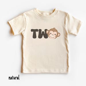 May include: A cream-colored toddler t-shirt with the word "TWO" in dark brown block letters and a cartoon monkey face. The word "natural" is printed in black at the bottom of the shirt.