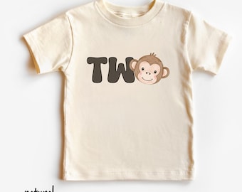 May include: A cream-colored toddler t-shirt with the word "TWO" in dark brown block letters and a cartoon monkey face. The word "natural" is printed in black at the bottom of the shirt.