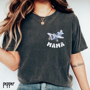 Pode incluir: T-shirt cinza escuro com um gr&aacute;fico de avi&atilde;o azul claro e a palavra "MAMA" em branco. A camisa tem gola redonda e mangas curtas. A palavra "pepper" est&aacute; impressa no canto inferior esquerdo.