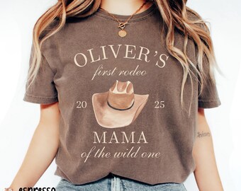 May include: A brown t-shirt with the text "OLIVER'S first rodeo 20 25 MAMA of the wild one" printed on it. A brown cowboy hat is illustrated above the text.