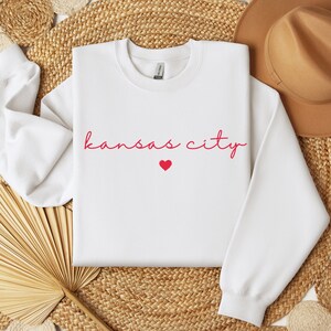 May include: White sweatshirt with the text "kansas city" in red cursive lettering and a small red heart.