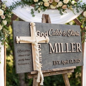 May include: A wooden wedding sign with the names "Caleb & Olivia Miller" and the date "April 12, 2025". The sign features a cross and a quote from Ecclesiastes. The sign is displayed on a wooden easel, with floral arrangements in the background.