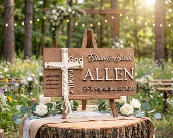 May include: A wooden wedding sign on a wooden easel, featuring a cross and the names "Ethan & Sarah Allen" with the date "September 12, 2024." The sign is decorated with a rope cross and set on a tree stump.