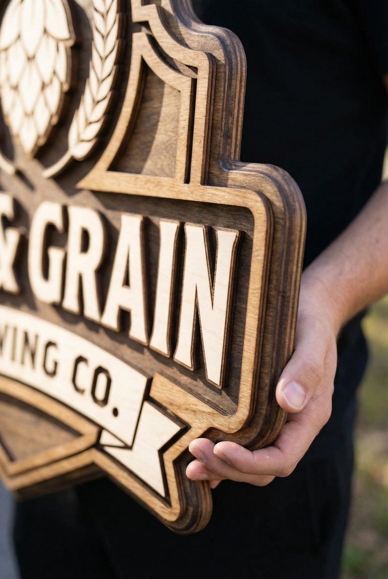 May include: A multi-layered wooden sign featuring a dark brown stained finish with light natural wood accents. The sign displays the text GRAIN and WING CO. along with a hop cone graphic. The design has a raised, dimensional structure.