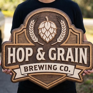 May include: A wooden sign with the words "HOP & GRAIN BREWING CO." in a layered design. The sign features a hop and wheat design at the top. The sign is held by a person.