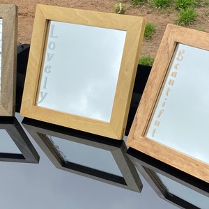 May include: Three wooden framed mirrors with the words "Gorgeous", "Lovely", and "Beautiful" etched into the glass. The mirrors are arranged in a row on a black surface.