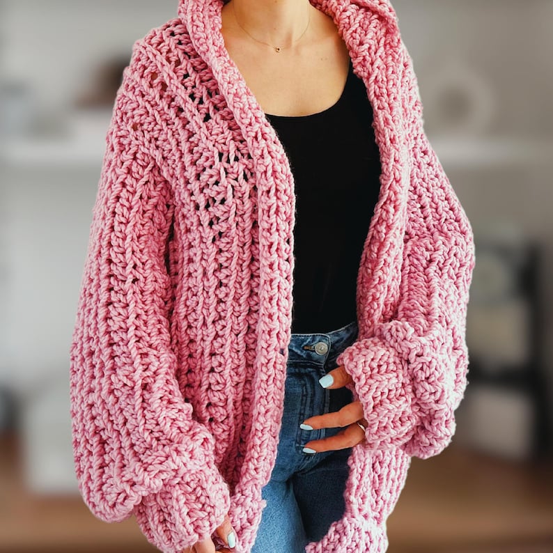 Op de afbeelding: Een roze gebreide cardigan met een losse pasvorm en lange mouwen. De cardigan heeft een V-hals en een capuchon.